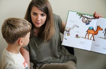 Adult holding open book with illustrations, looking at child
