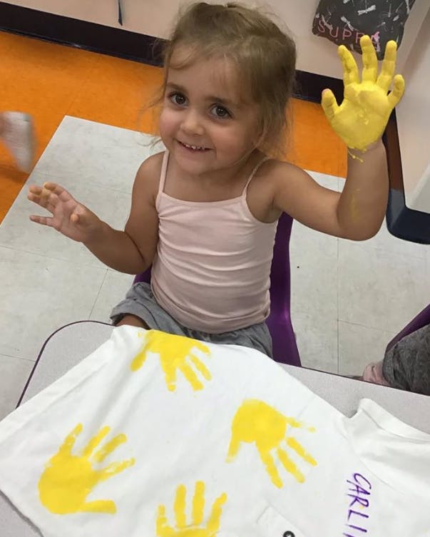 Child with yellow painted hand and handprints on a white shirt
