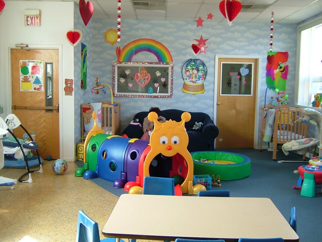 Playroom with colorful caterpillar tunnel, small table, and cribs