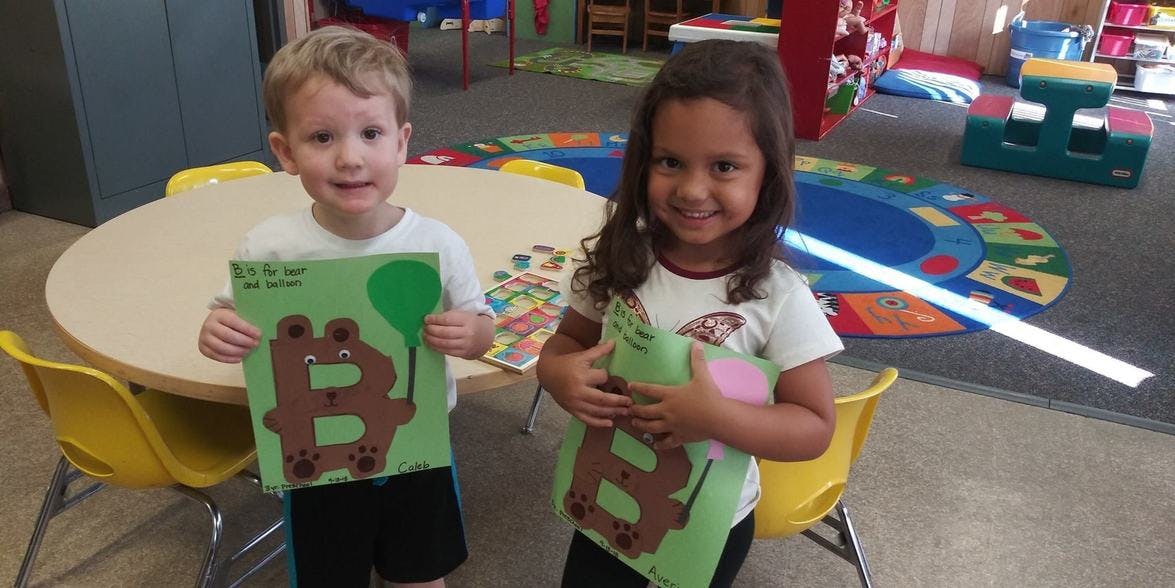 Two children holding up crafts with the letter B on them in a classroom