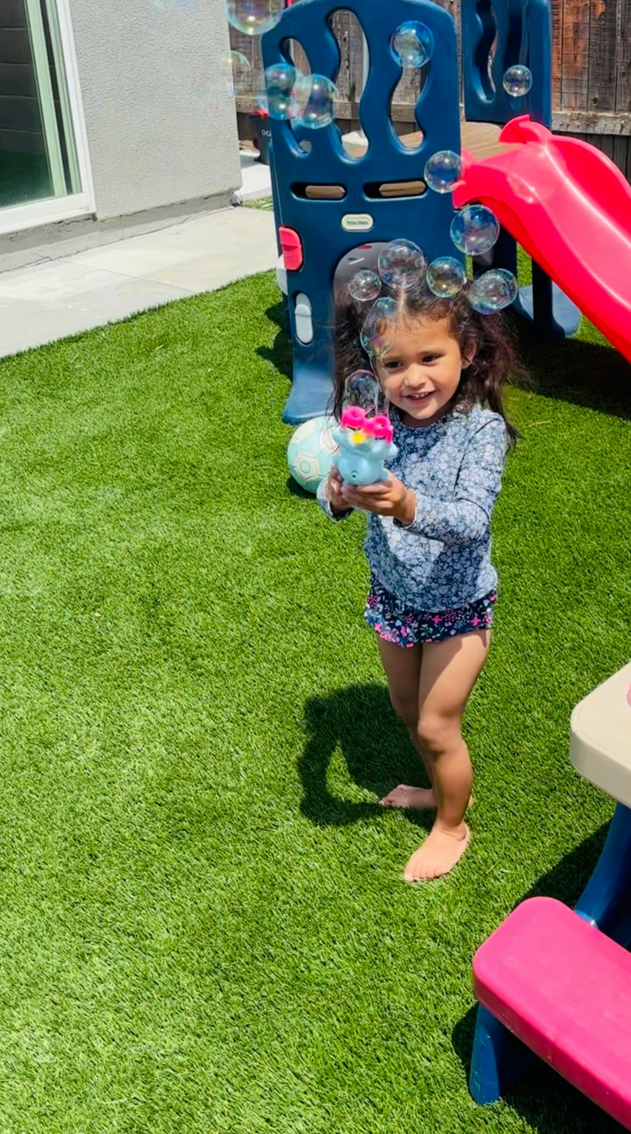 Child playing with a bubble machine on green grass