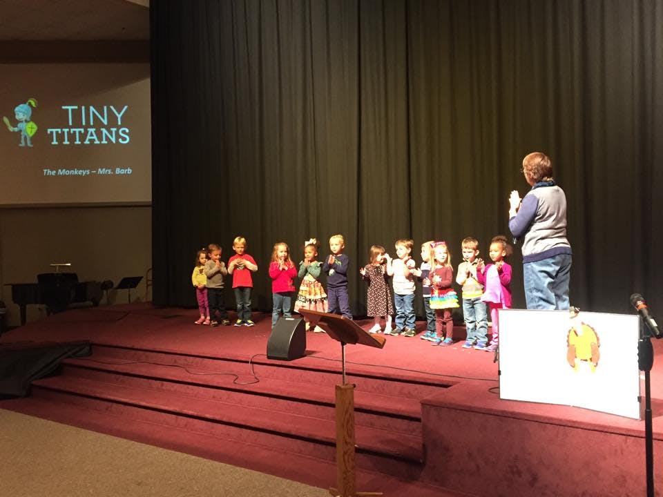 Person speaking to a group of children on a stage