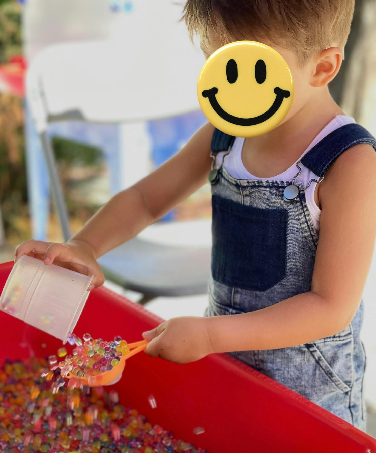 Child pouring colorful beads from a cup into a red bin with a scoop