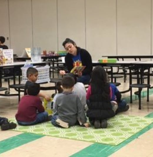 Person reading to a group of children sitting on a mat