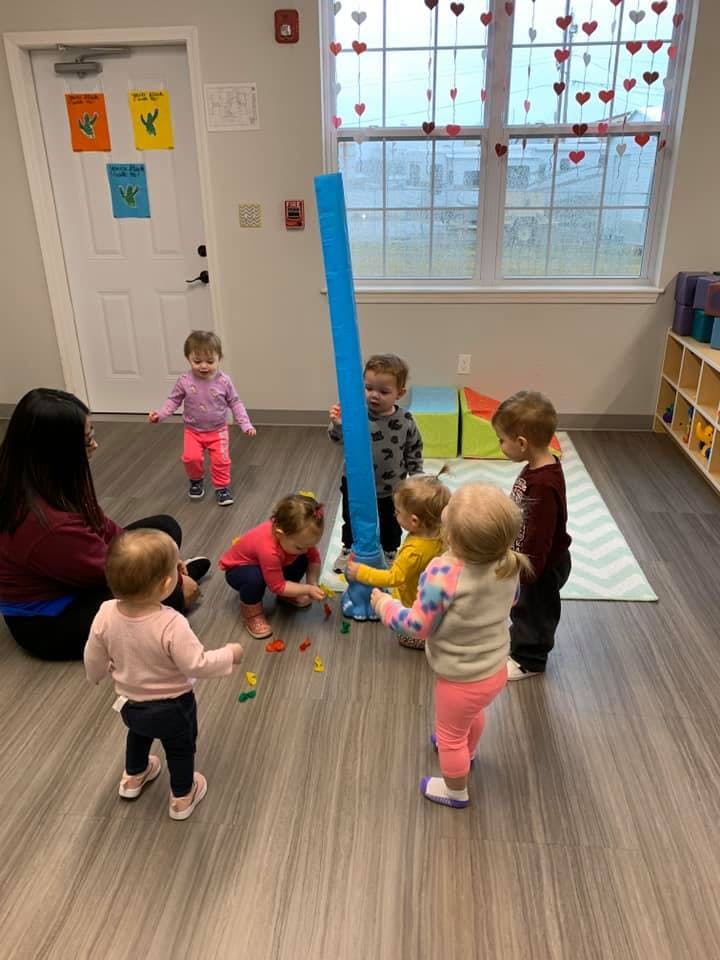 Adult and multiple children playing with a large blue tube and small colorful objects