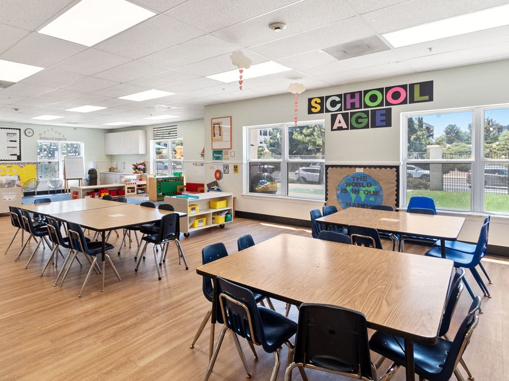 An empty classroom with tables, chairs, and large windows