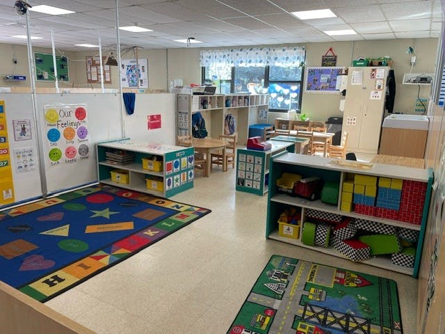 Empty classroom with colorful rugs and shelves filled with toys and learning materials