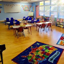 Empty classroom with small tables and chairs, map rug on floor