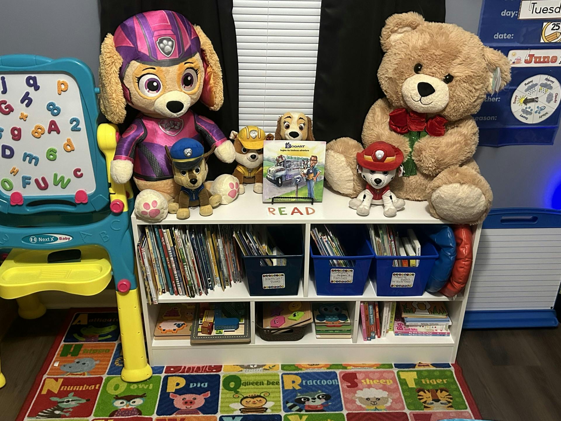 Stuffed animals on a bookshelf with books and an alphabet board
