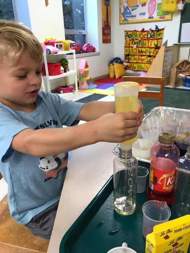 Child pouring liquid from a squeeze bottle into a clear bottle