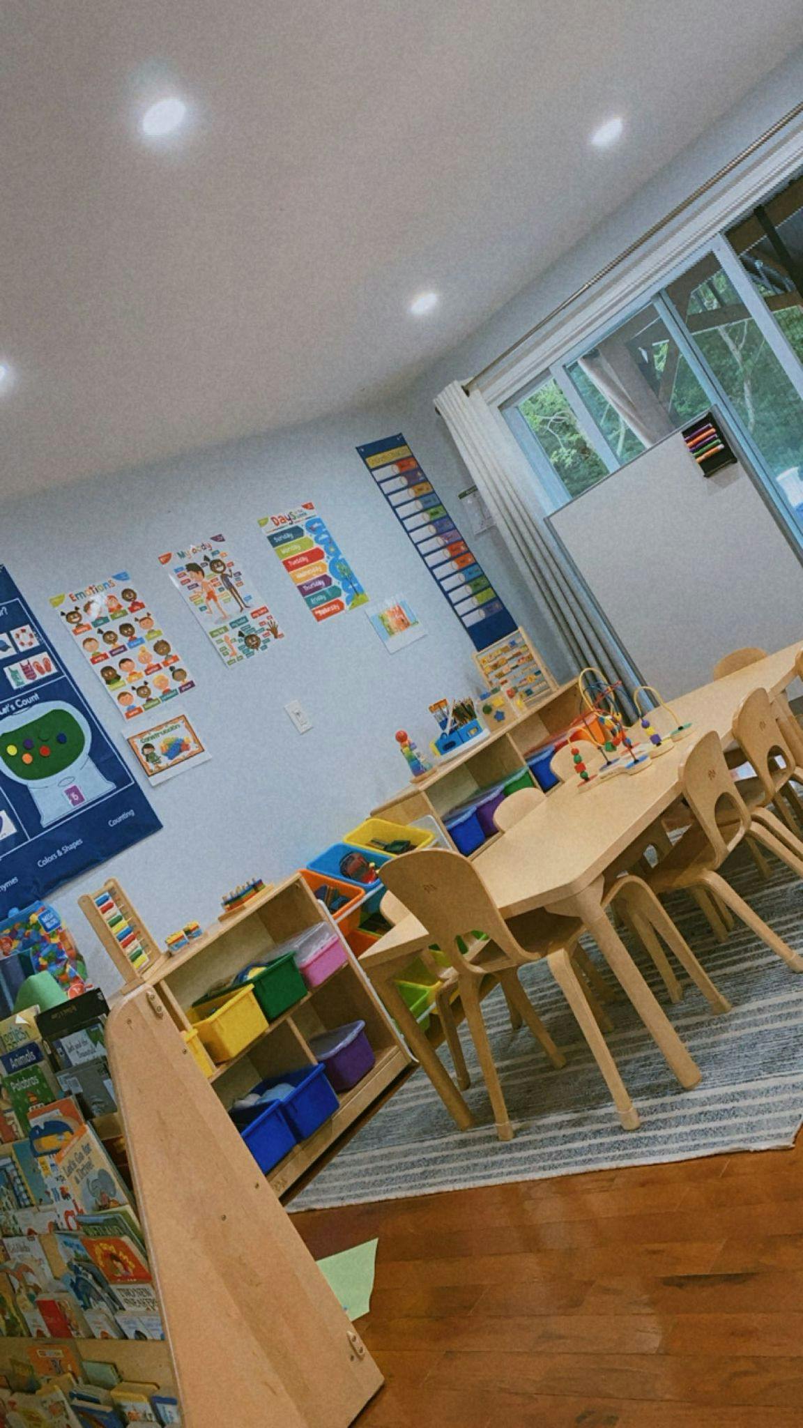 Classroom with small tables and chairs, shelves with colorful bins, and wall decorations