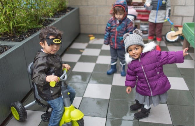 Child in Batman mask on tricycle with other children on a patio