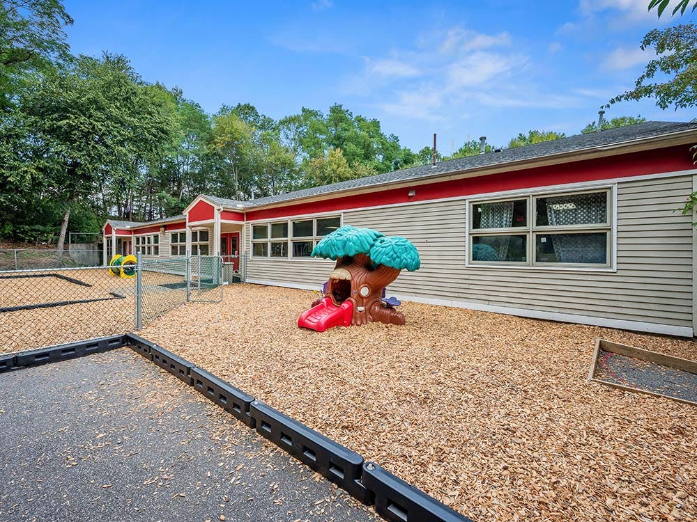 Playground with wood chips and treehouse slide next to a building