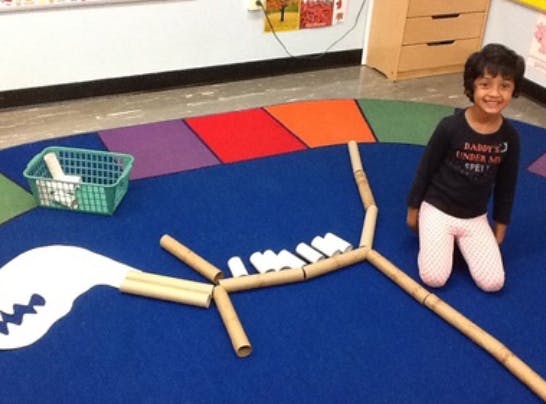 Child kneeling next to a dinosaur skeleton made from cardboard tubes