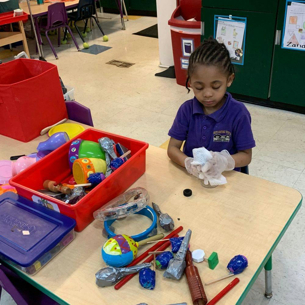 Child wearing gloves and holding an object at a table with toys
