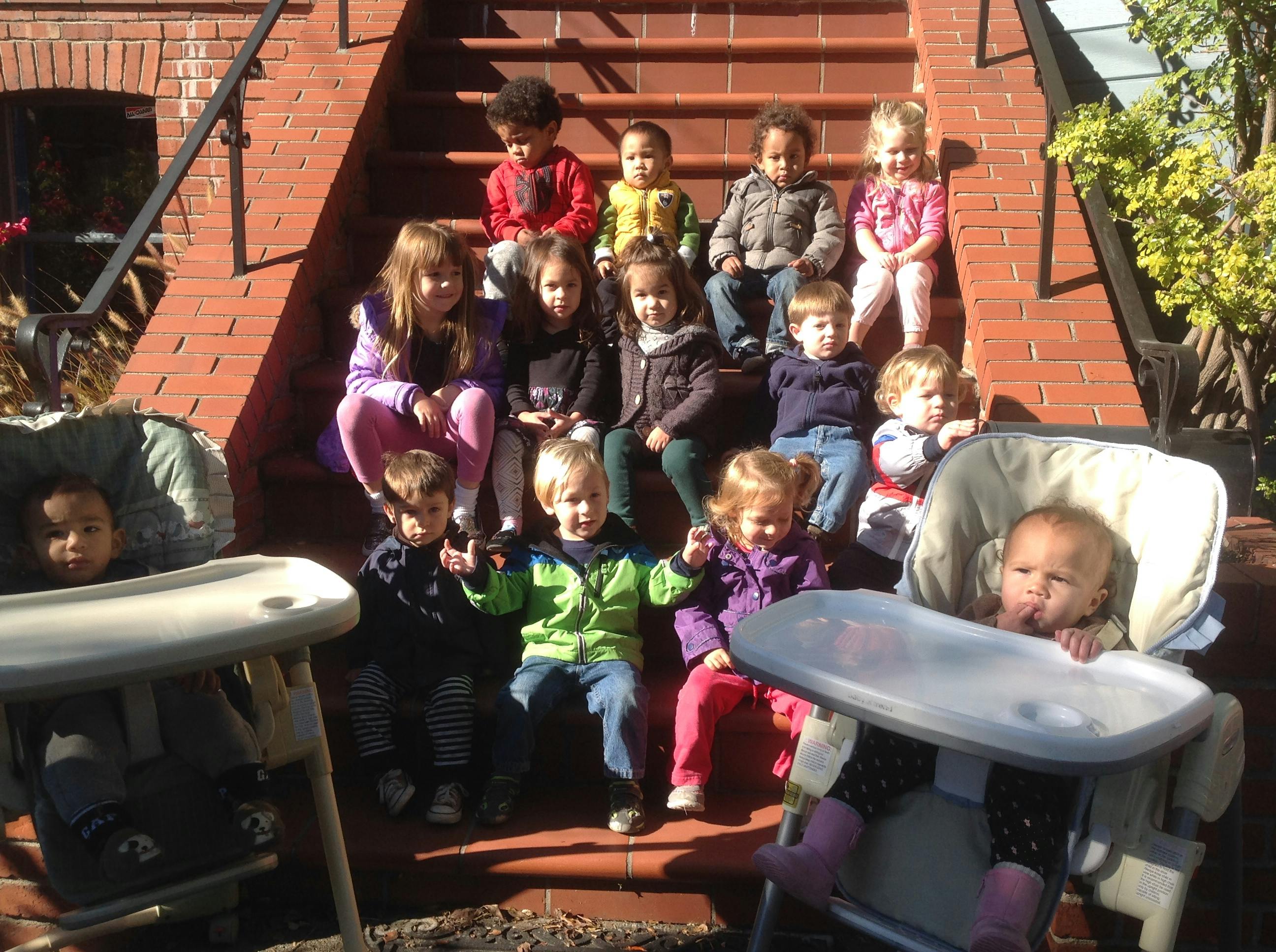 Group of children sitting on brick steps with two toddlers in high chairs