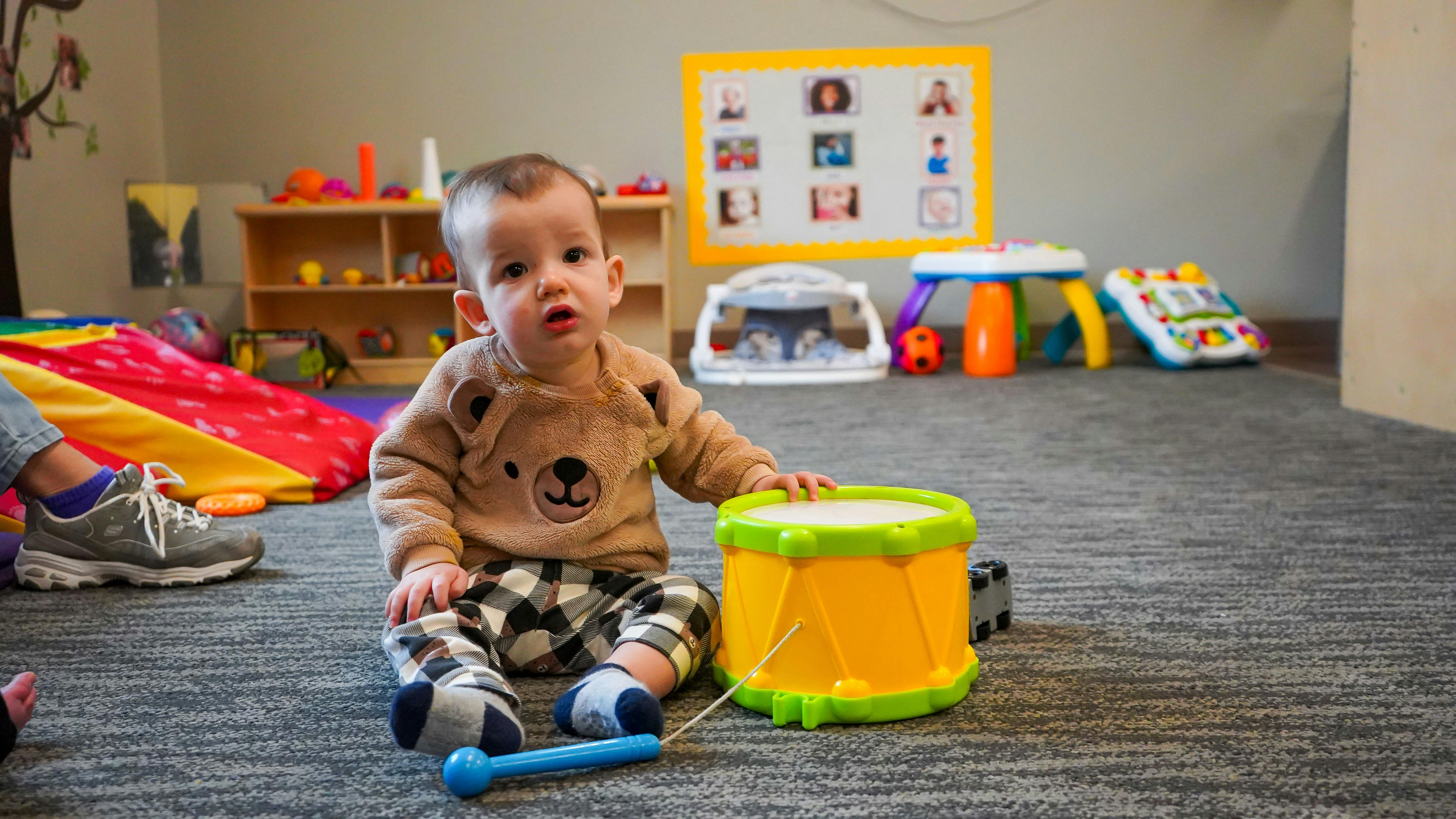 Child sitting on floor next to a toy drum