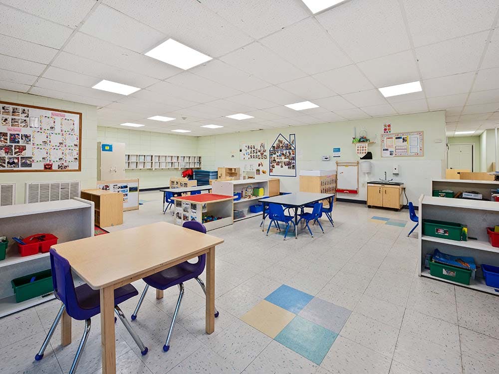 Empty classroom with small tables and chairs, storage shelves, and bulletin boards