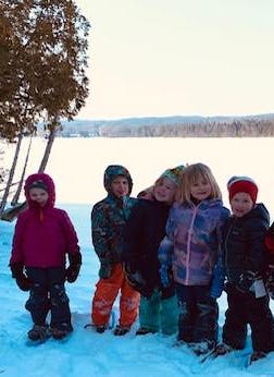 Five children standing in snow with a frozen lake in the background