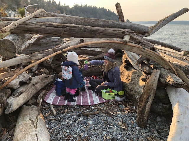 Two people sitting on a blanket under a driftwood structure on a beach