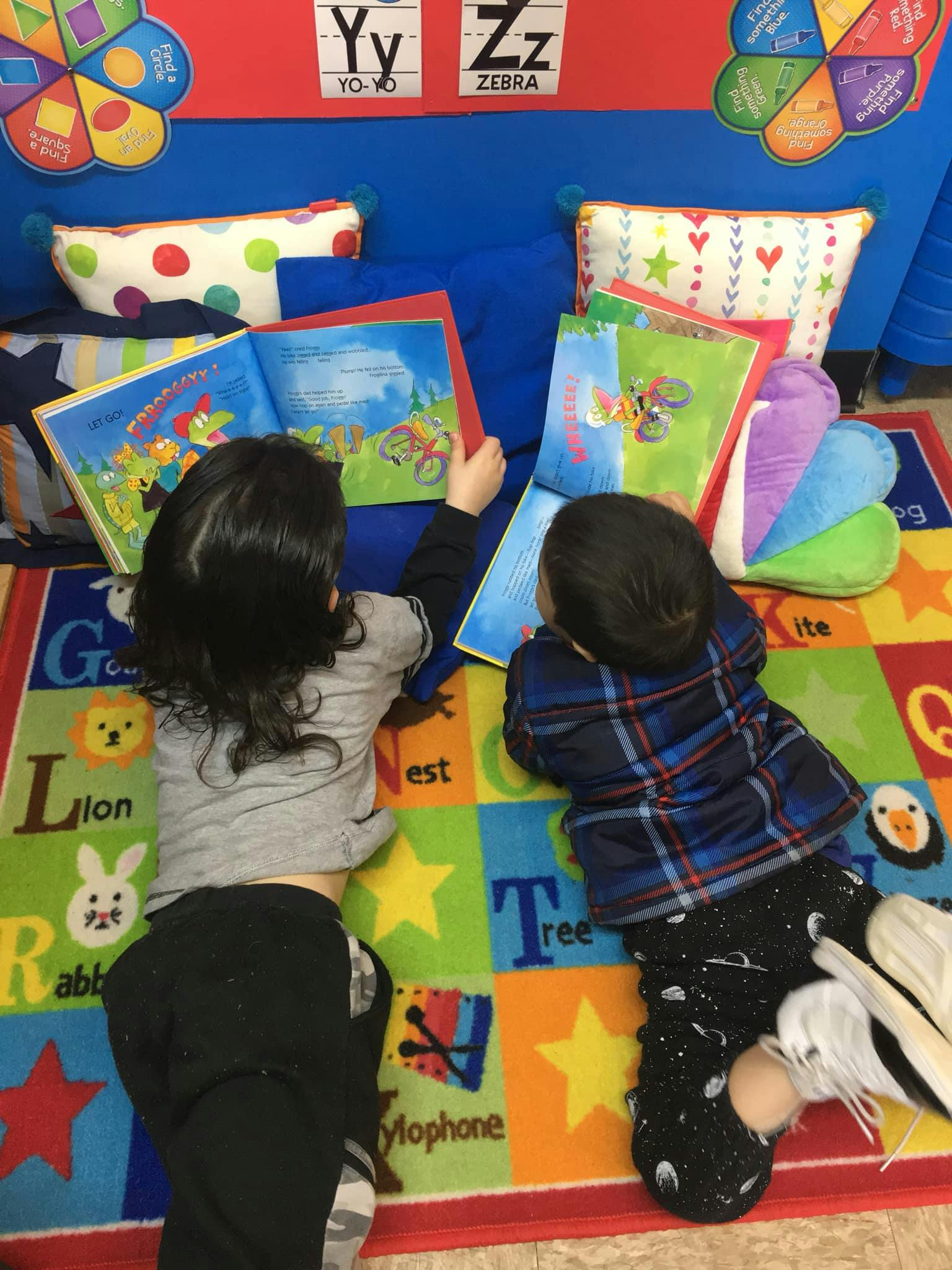 Two children lying on a colorful rug reading books