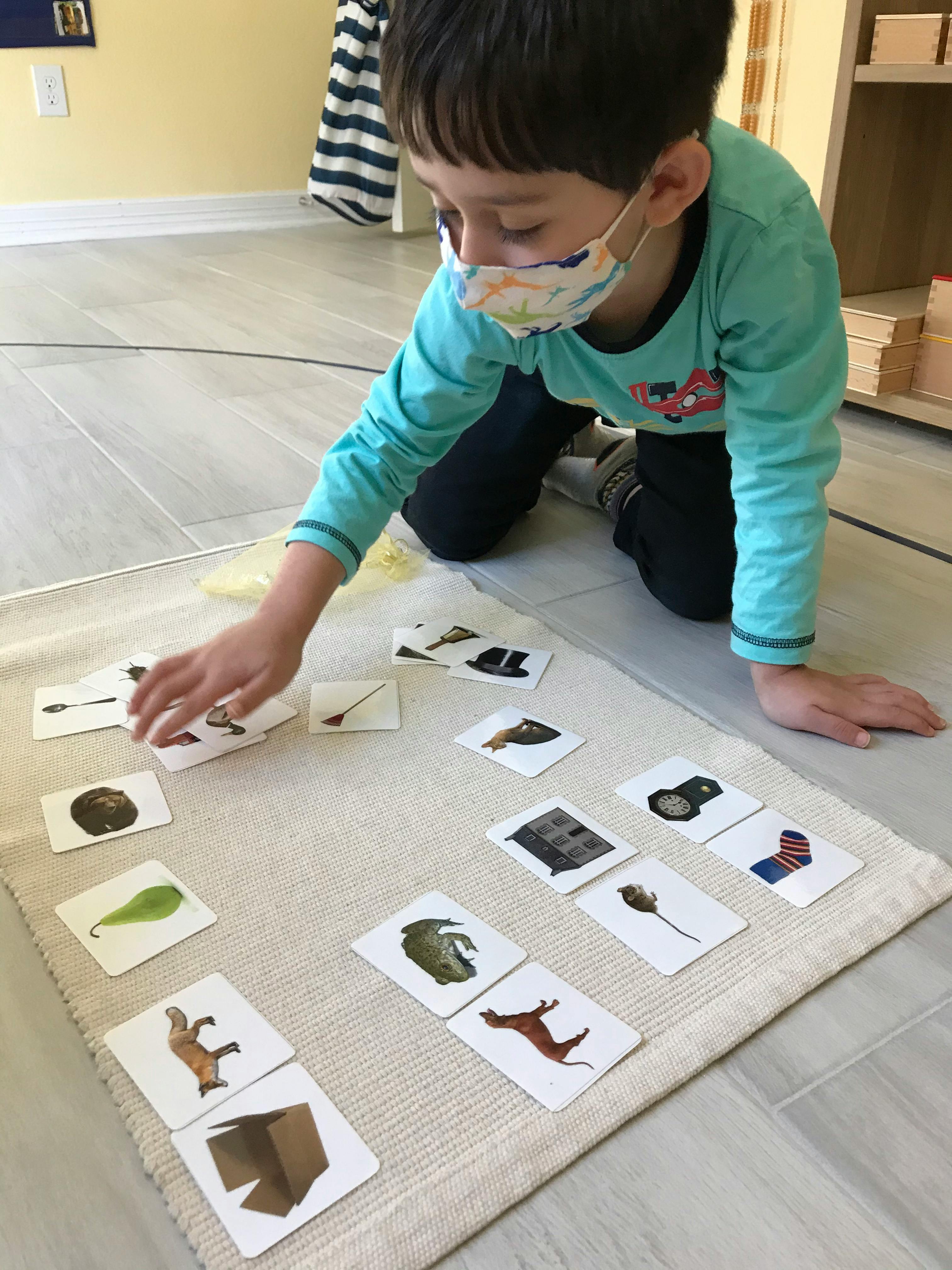Child in a face mask playing with picture cards on a rug