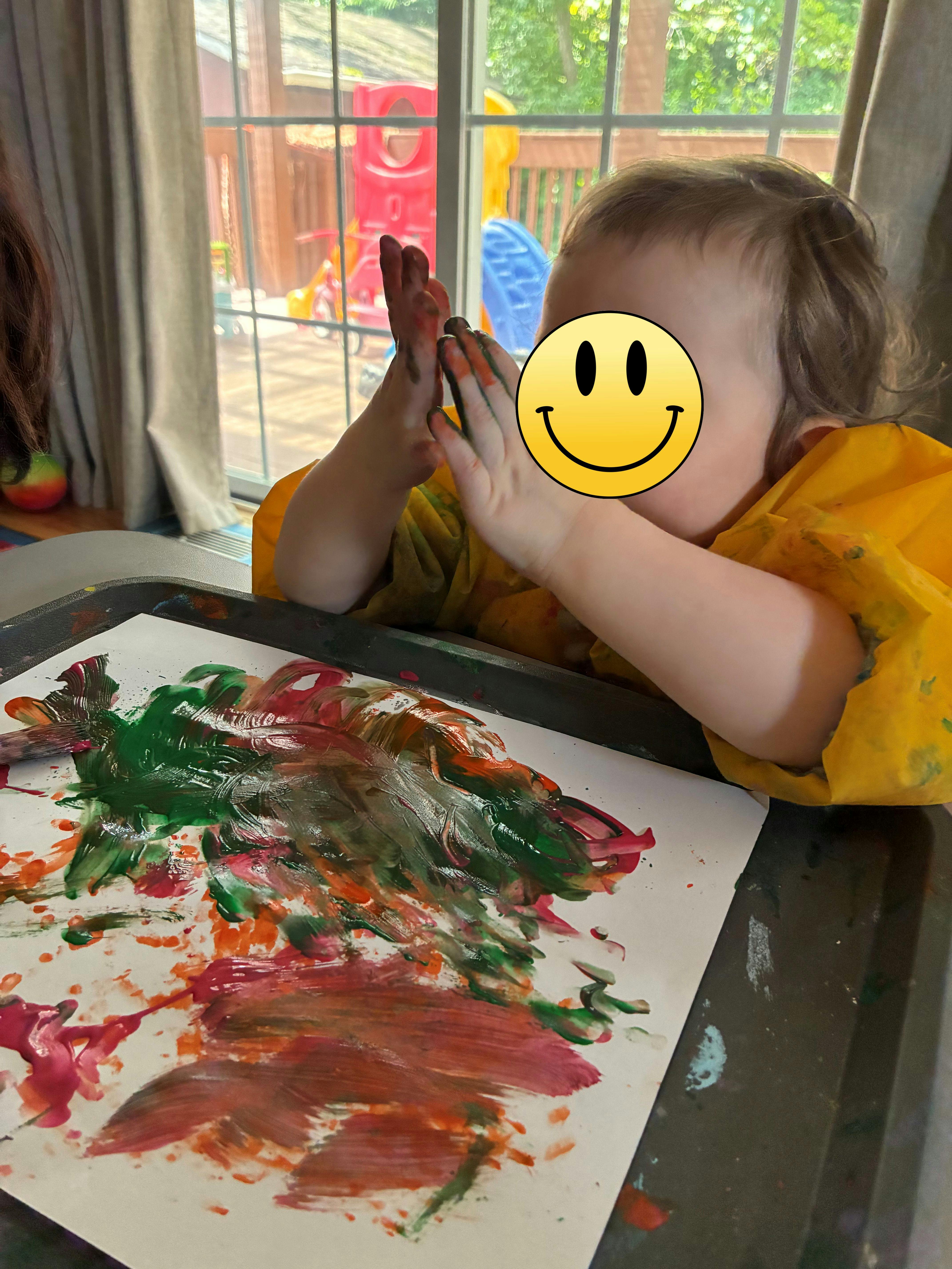 Child wearing an apron painting with hands on paper at a table