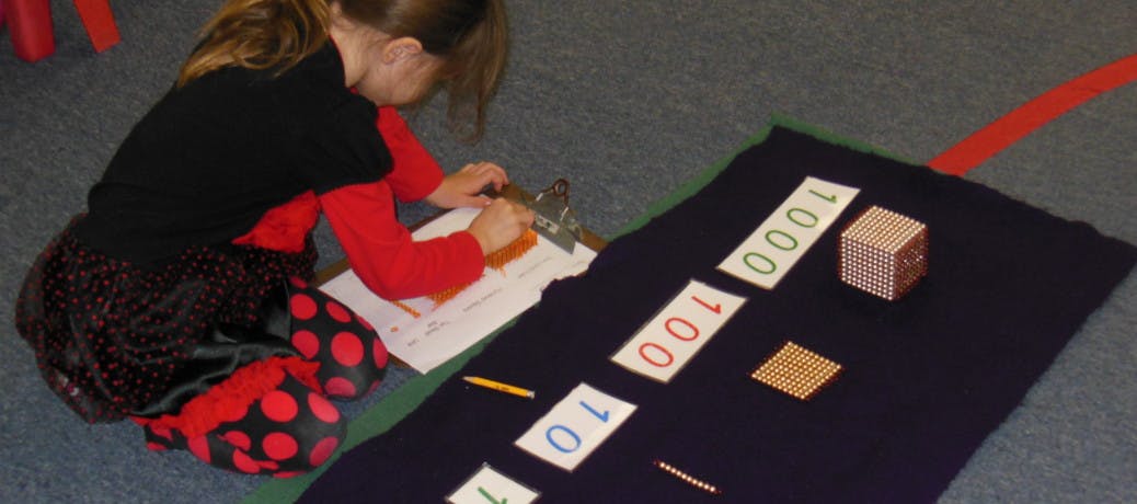 Child writing on paper next to number cards on a mat