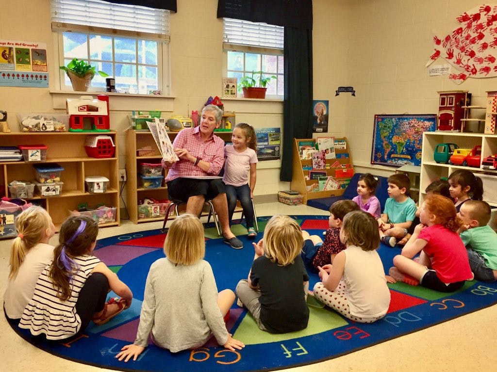 Adult reading a book to a group of children in a classroom