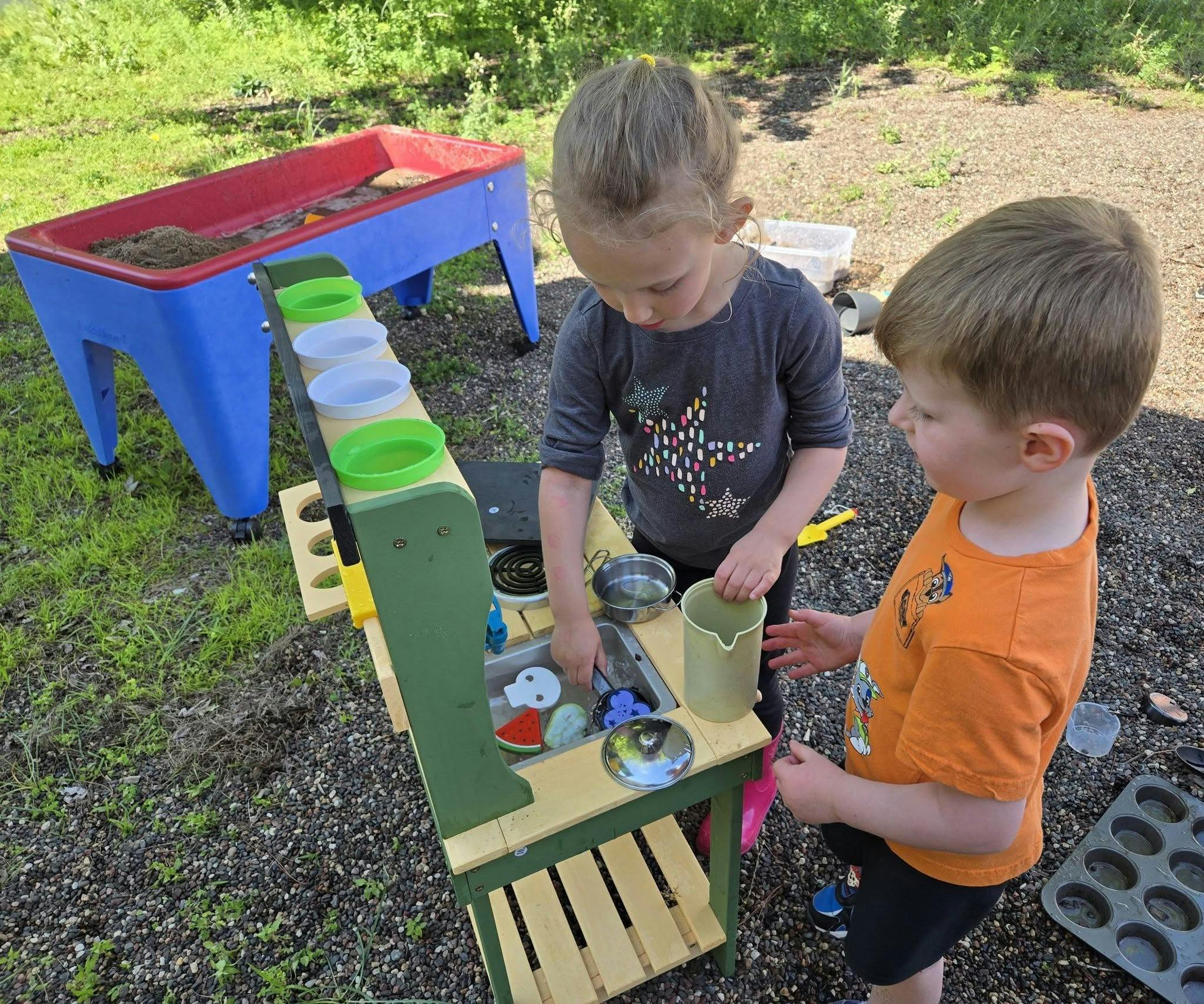 Two children playing with a toy kitchen outdoors