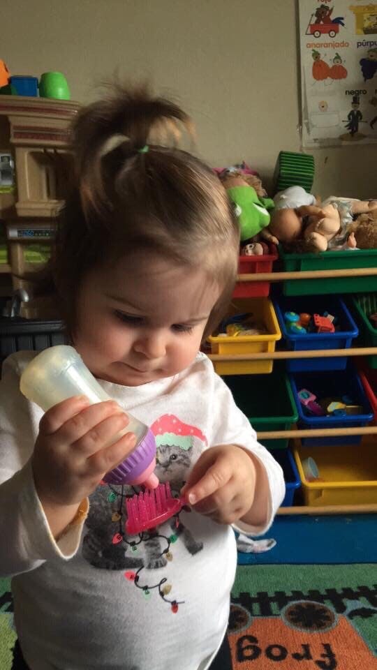 Child holding a baby bottle and a small pink brush