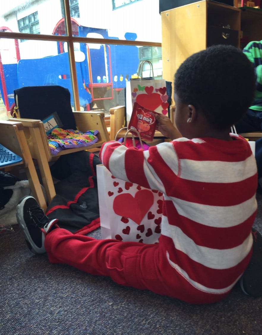 Child sitting on floor, holding a small bag with a heart design