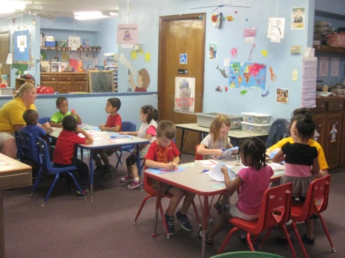 Adult and children sitting at tables in a classroom