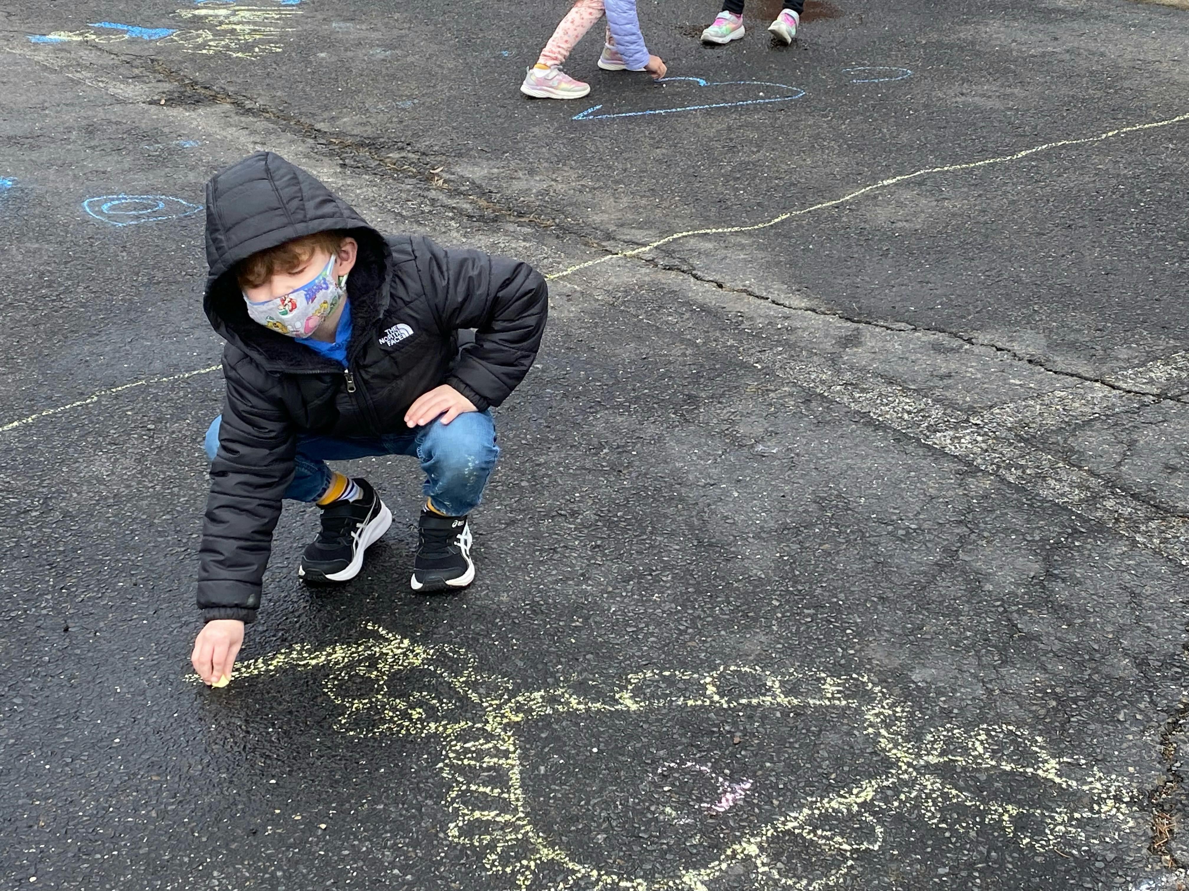 Child in a mask drawing with chalk on pavement