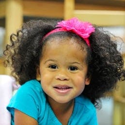 Child with curly hair and a pink headband smiling