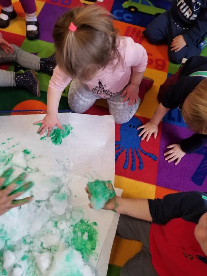 Children playing with green paint and white foam on paper