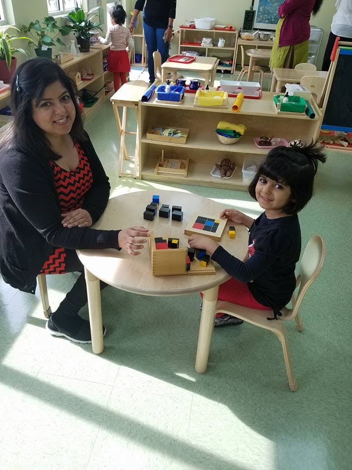 Adult and child playing with blocks at a table in a classroom