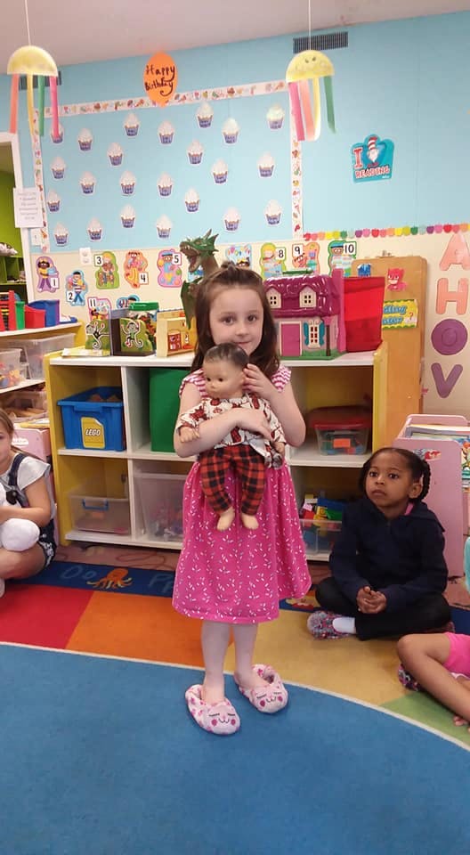 Child in pink dress holding a doll in a classroom