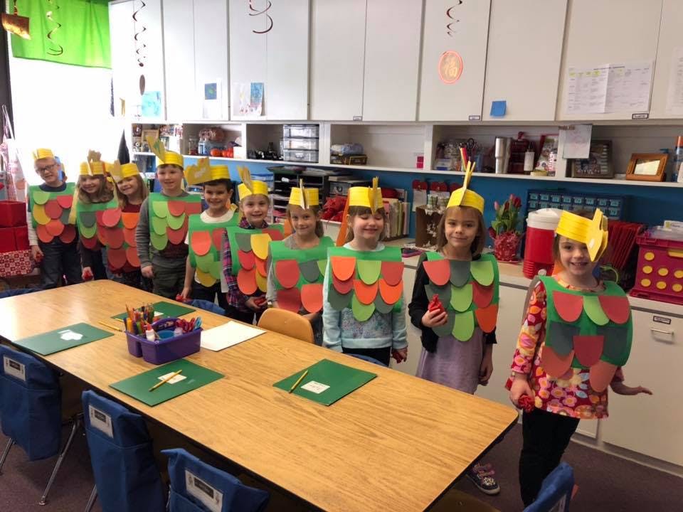 Children in a classroom wearing costumes with yellow hats and scale-like vests