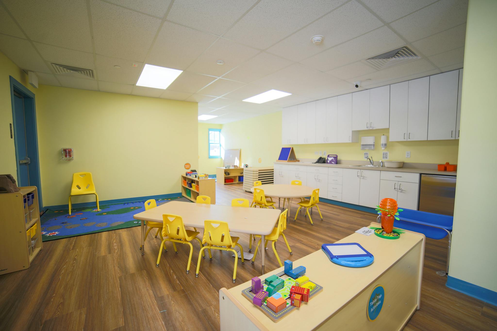 Classroom with small tables and chairs, and a counter with cabinets