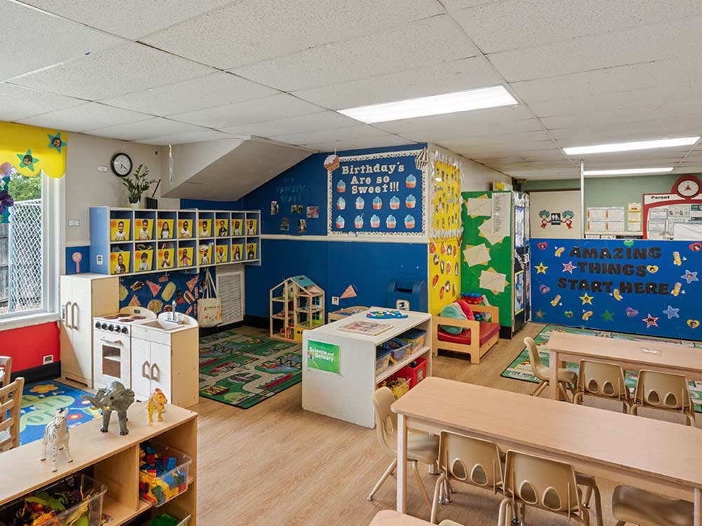 Children's classroom with small tables and chairs, shelves, play kitchen, and wall decorations