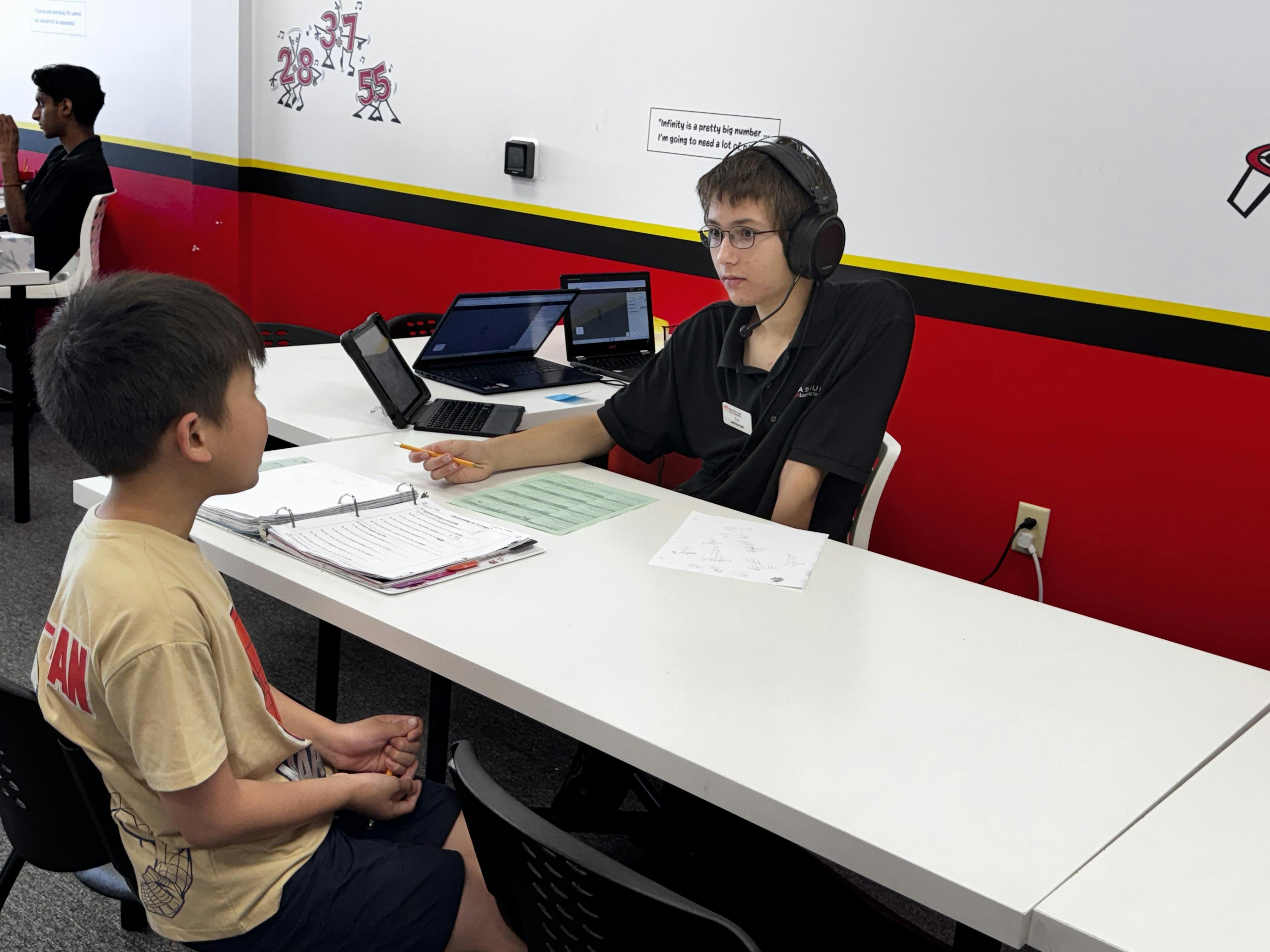Person with headphones and child at a table with papers and laptops