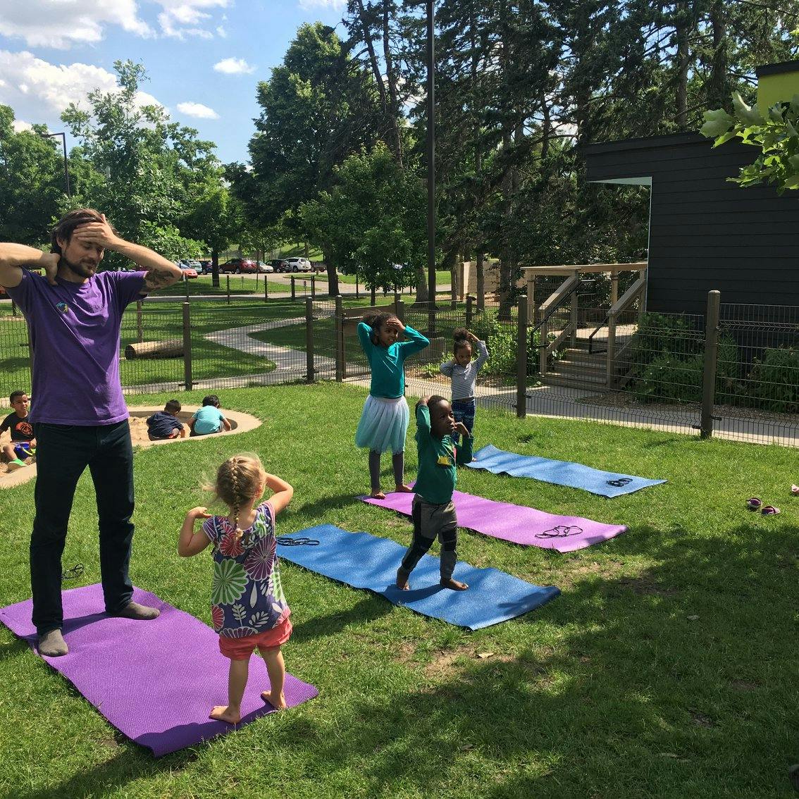 Adult and children doing yoga outdoors on mats