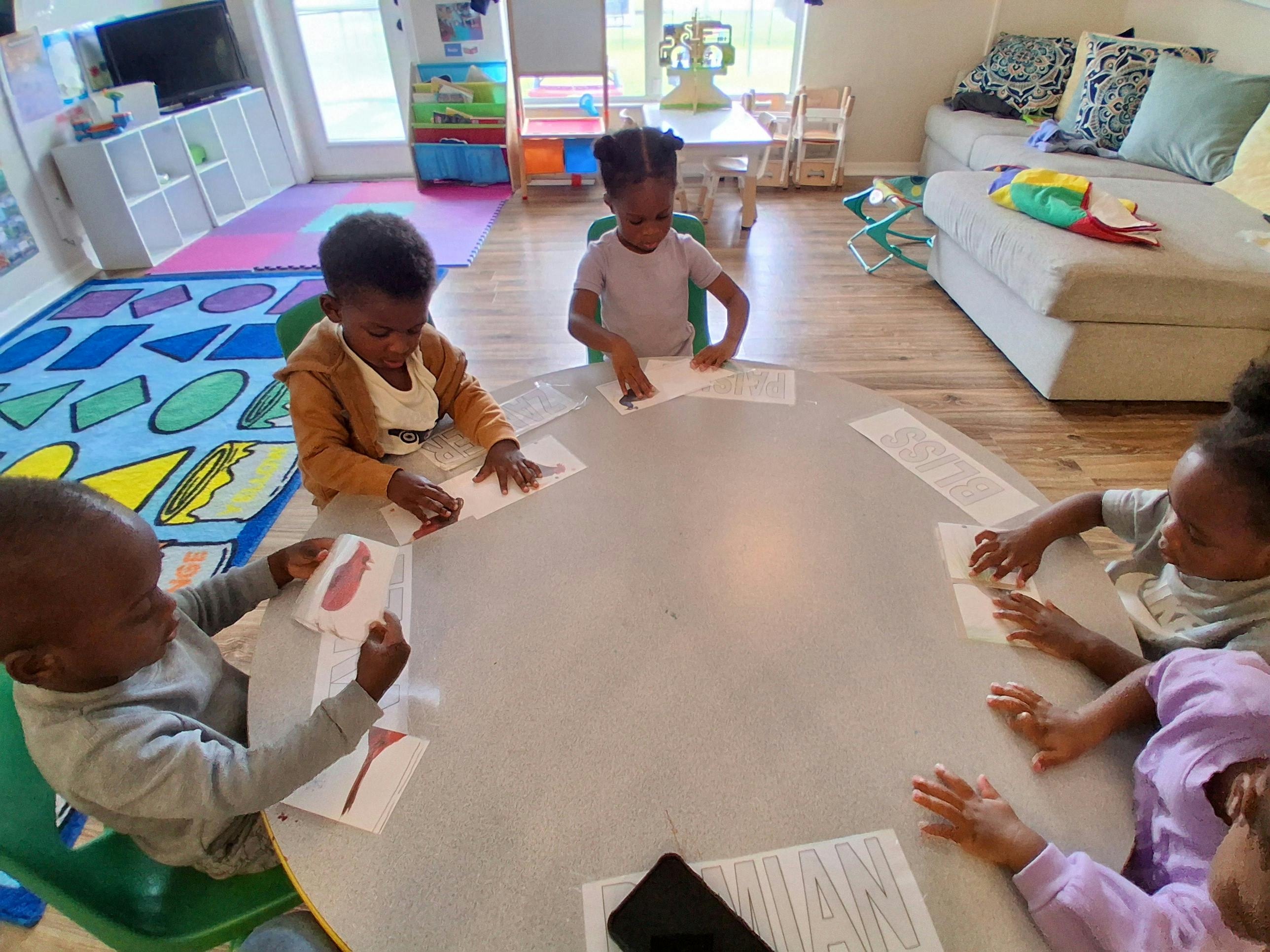 Four children at a table playing with papers in a classroom