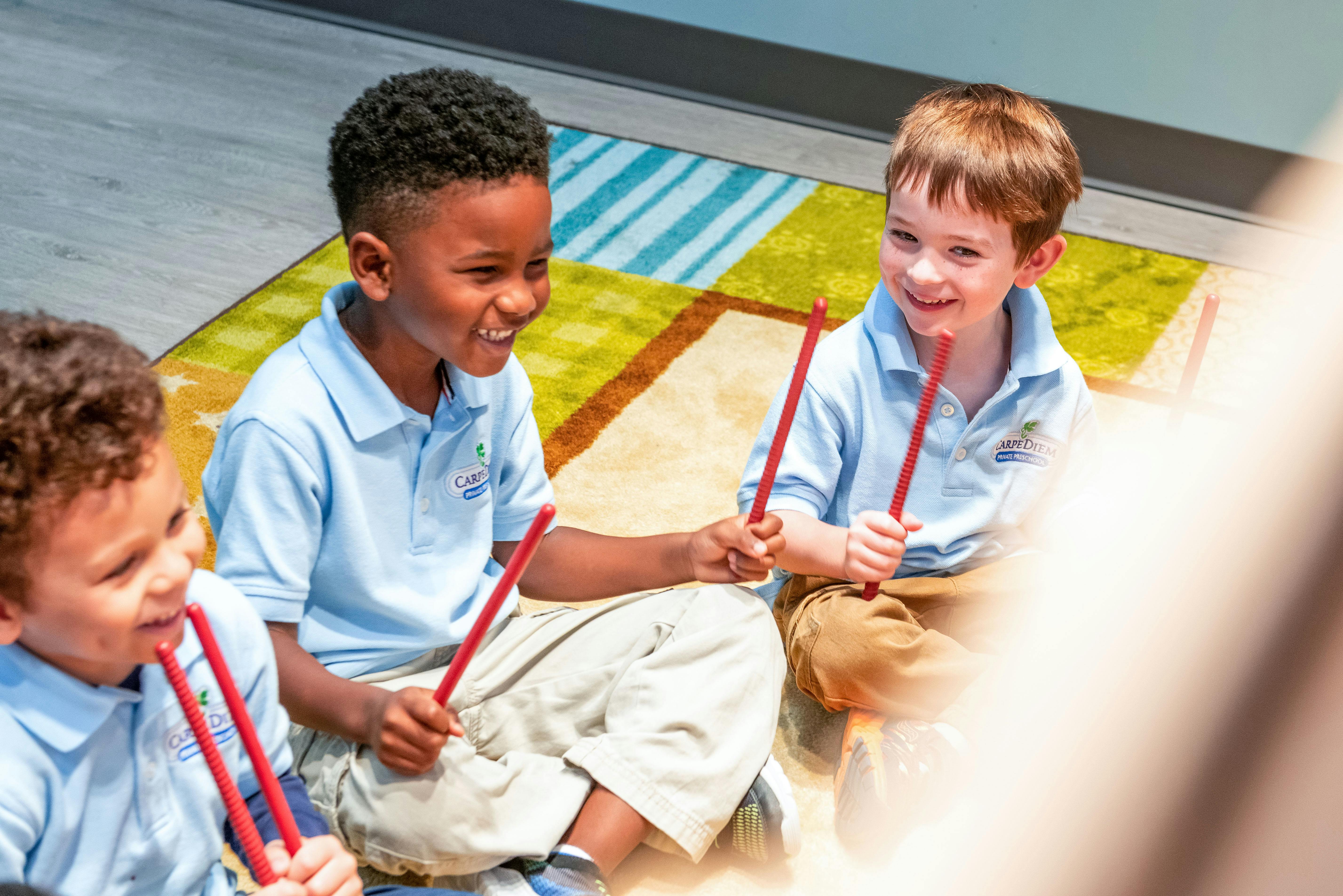 Three children sitting on a rug holding red drumsticks