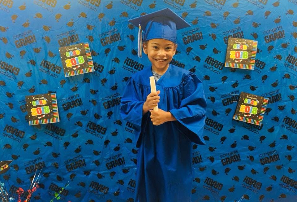 Child in blue graduation cap and gown holding a rolled diploma