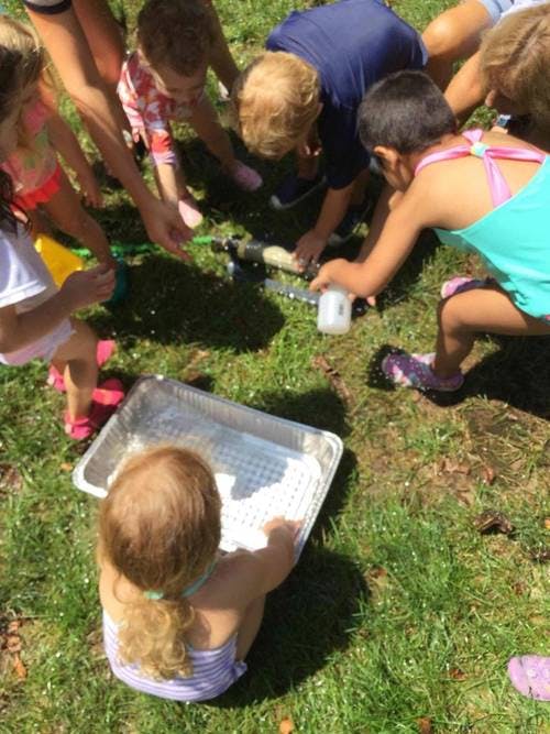 Children playing with water and a tray on grass