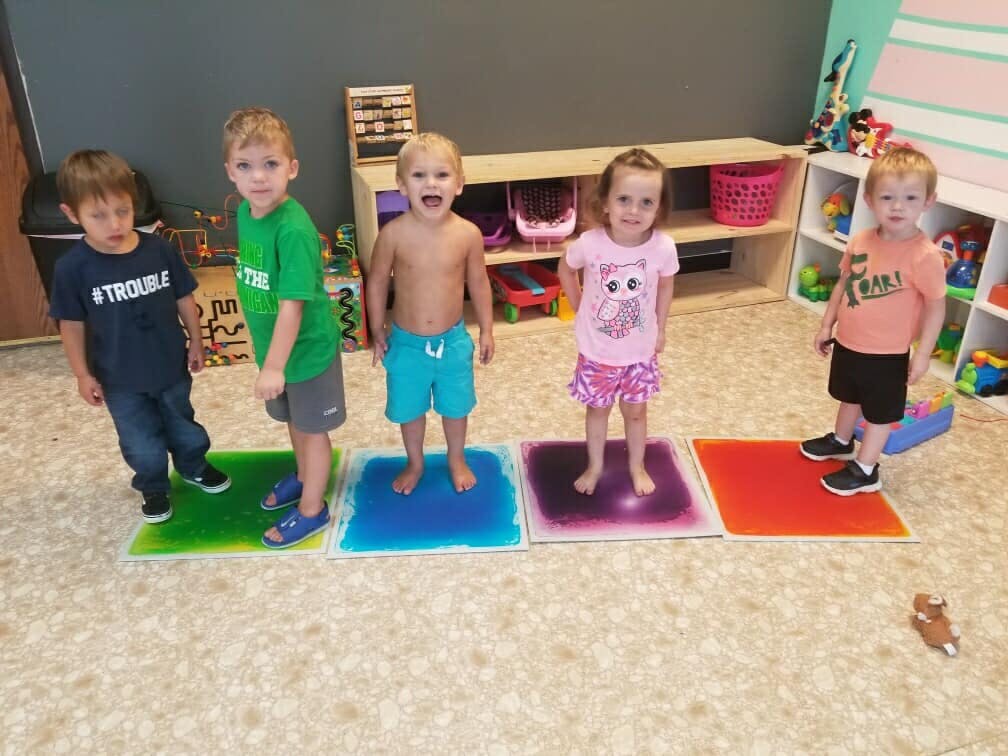 Five children standing on colorful liquid floor tiles