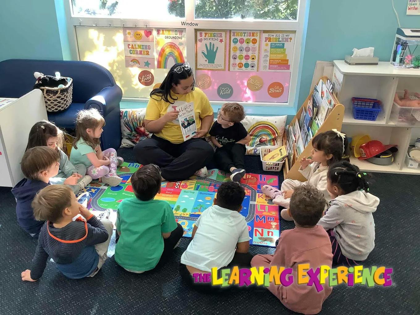 Person reading a book to a group of children sitting on a colorful mat
