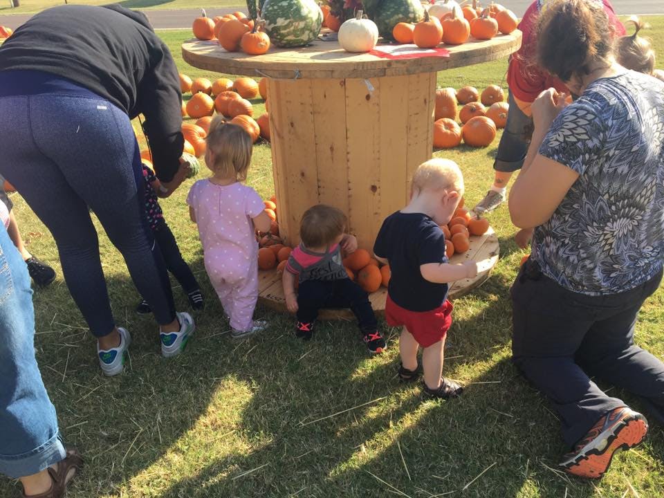 People and children around a wooden spool table with pumpkins